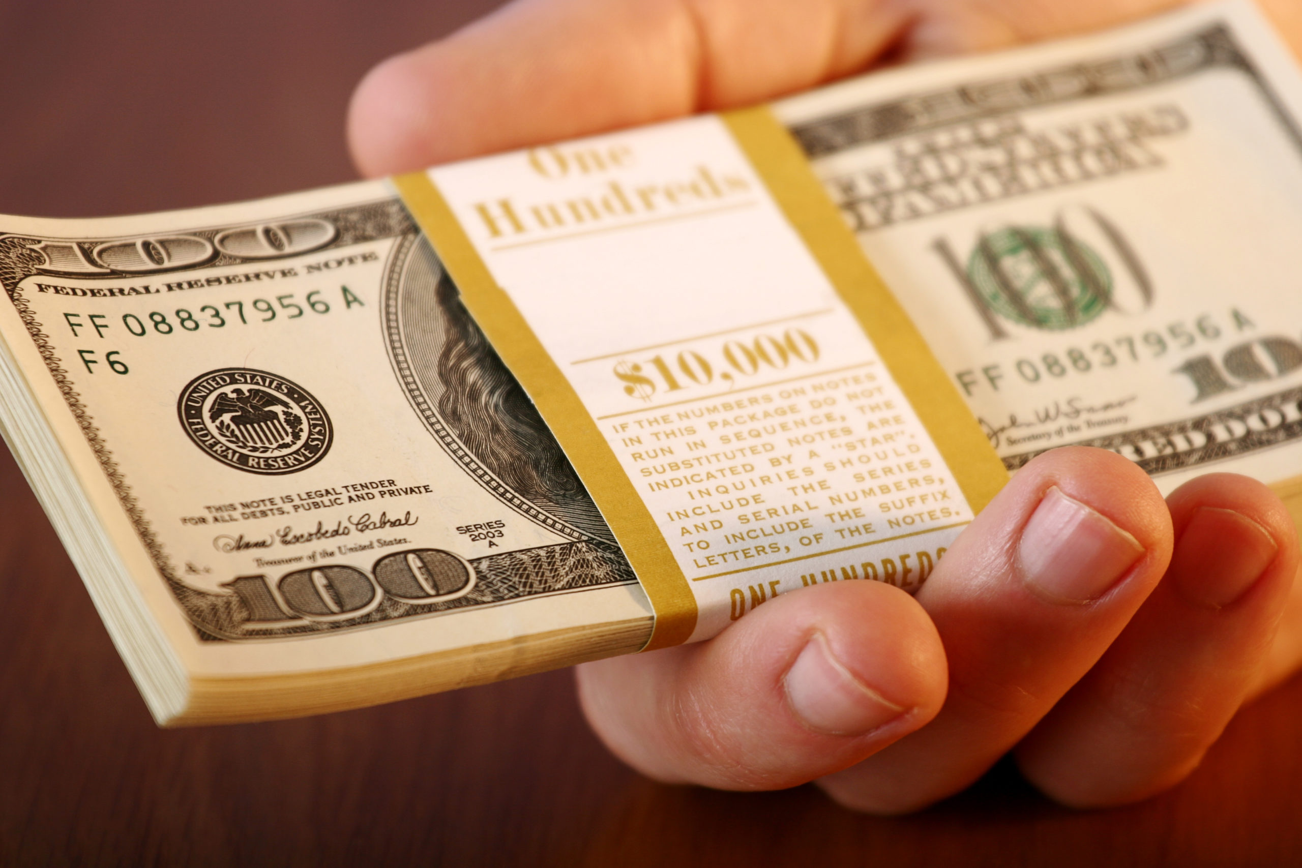 Close-up of mans hand holding out $10,000